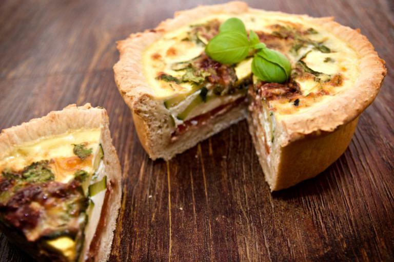 Un delicioso quiche mediterráneo de capas profundas con guarnición de albahaca.