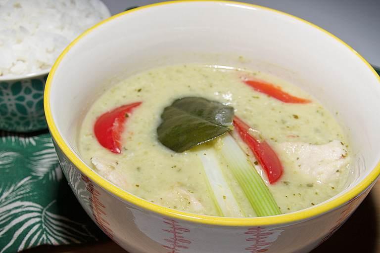 Un tazón tradicional de curry verde tailandés aromático y cremoso, con trozos de pollo y verduras.